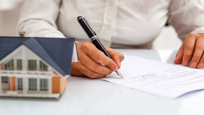 la main d'un homme signant un document à côté d'une maquette de maison sur une table - domiciliation de société - Activ Solutions