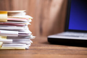 une pile de fichiers sur un bureau avec un laptop en arrière-plan - externalisation gestion administrative Madagascar - Activ Solutions